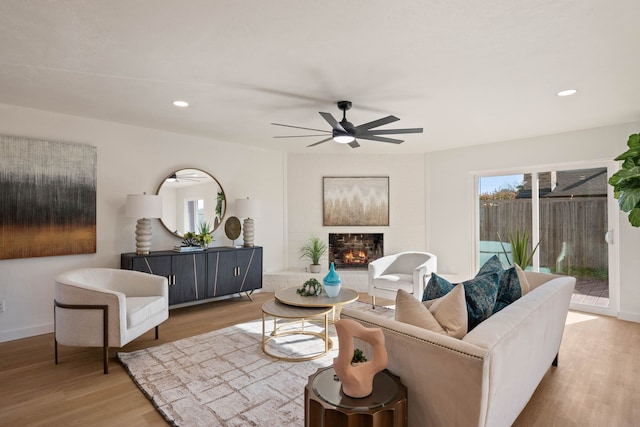 living room featuring light wood-type flooring, ceiling fan, recessed lighting, and a lit fireplace