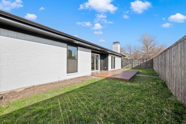 rear view of house with brick siding, a lawn, a chimney, and a fenced backyard