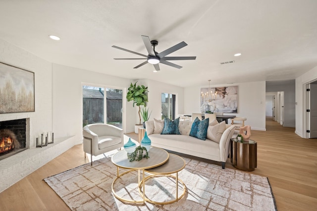living area featuring recessed lighting, visible vents, a fireplace, light wood-style flooring, and ceiling fan with notable chandelier