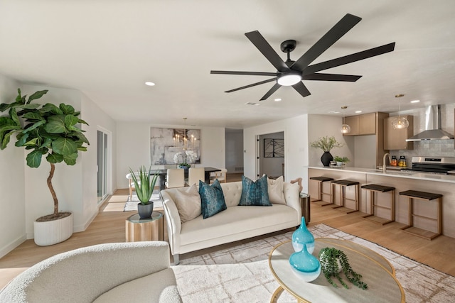living area featuring light wood-type flooring, baseboards, recessed lighting, and ceiling fan with notable chandelier