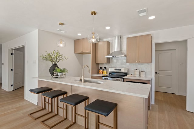 kitchen featuring visible vents, wall chimney range hood, a sink, light wood-style floors, and stainless steel electric range oven