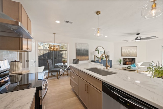 kitchen featuring wall chimney exhaust hood, a sink, light wood-type flooring, visible vents, and appliances with stainless steel finishes