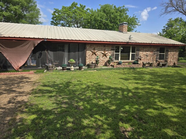 back of house featuring a chimney, brick siding, a yard, and metal roof