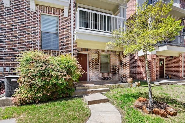 doorway to property with brick siding, central air condition unit, and a balcony