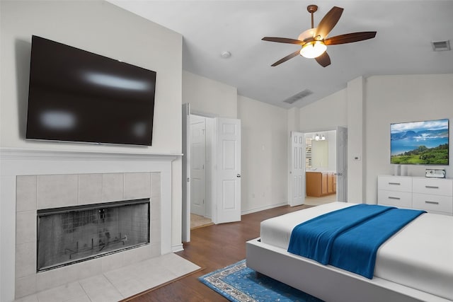 bedroom with a tile fireplace, visible vents, lofted ceiling, and wood finished floors