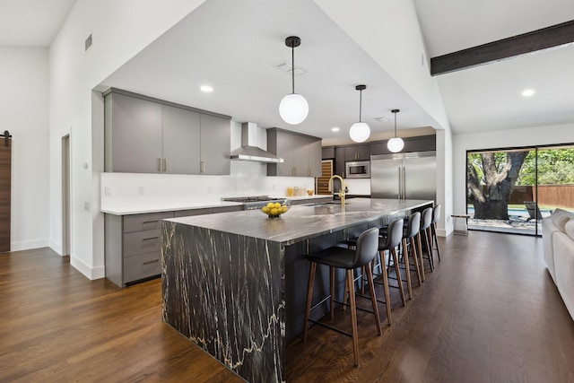 kitchen featuring wall chimney range hood, a sink, built in appliances, gray cabinetry, and dark wood-type flooring