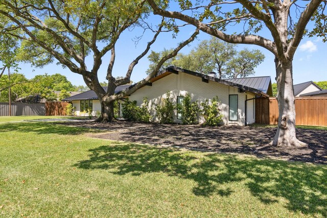 view of front facade featuring fence, brick siding, a front yard, and metal roof