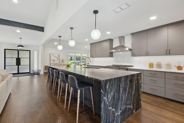 kitchen with a large island, visible vents, gray cabinets, a sink, and wall chimney exhaust hood