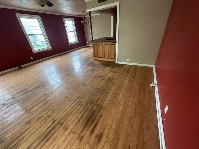 empty room with crown molding, hardwood / wood-style floors, a ceiling fan, and baseboards