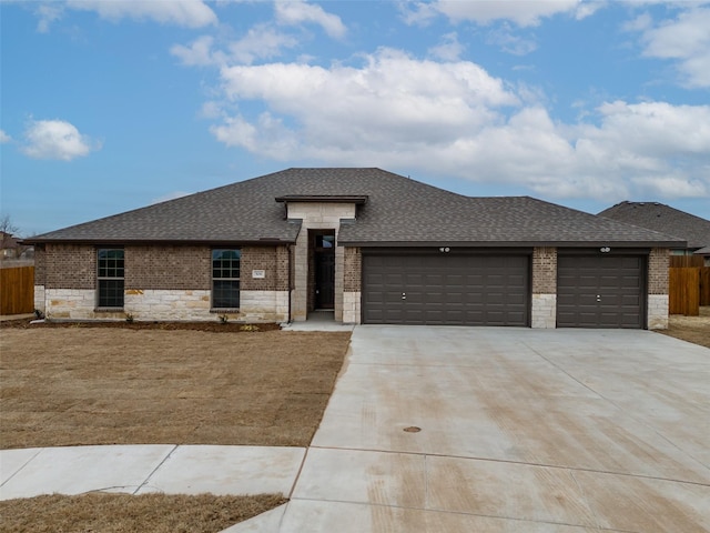 prairie-style home featuring fence, a shingled roof, and a garage