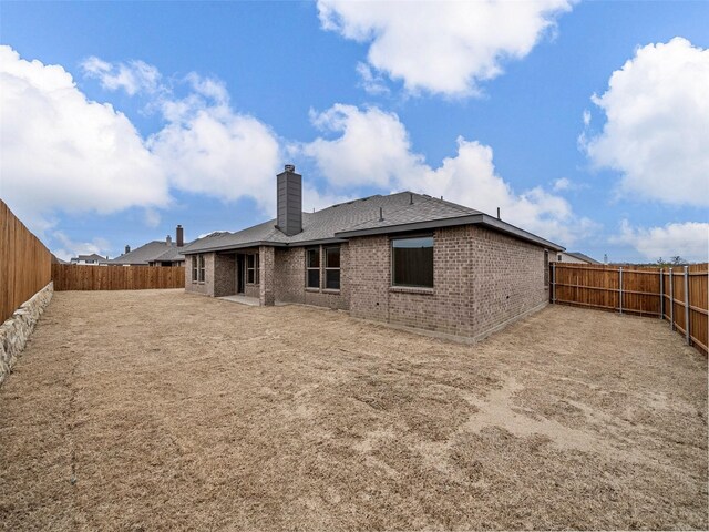 rear view of property with a fenced backyard, a chimney, and brick siding