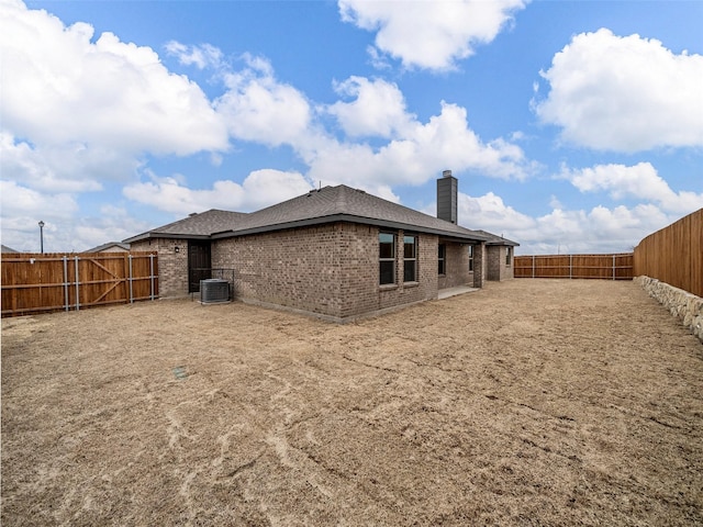 rear view of house featuring cooling unit, brick siding, a fenced backyard, and a chimney