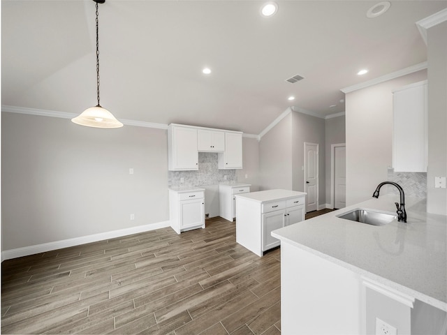 kitchen featuring a sink, backsplash, white cabinetry, wood finished floors, and crown molding