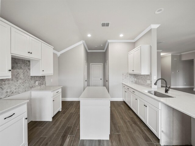 kitchen with a sink, baseboards, visible vents, backsplash, and crown molding