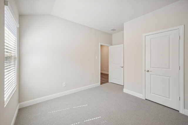 unfurnished bedroom featuring lofted ceiling, visible vents, carpet flooring, and baseboards