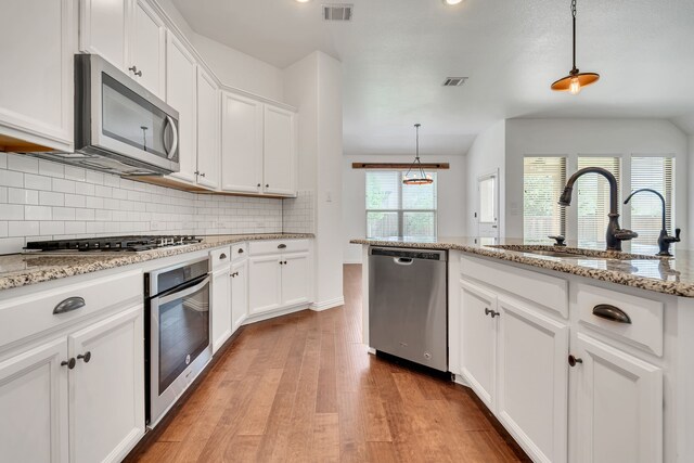 kitchen featuring decorative backsplash, stainless steel appliances, light wood-type flooring, a sink, and visible vents