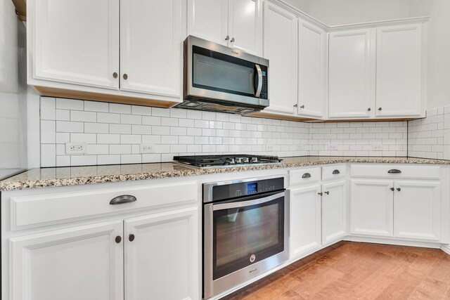 kitchen with white cabinetry, backsplash, appliances with stainless steel finishes, and light stone counters