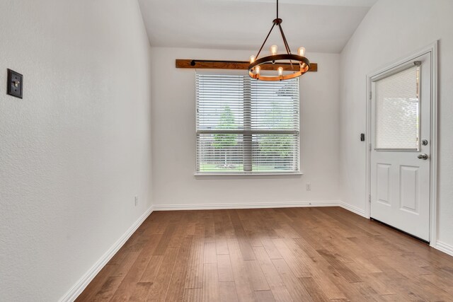 unfurnished dining area featuring an inviting chandelier, wood finished floors, and baseboards
