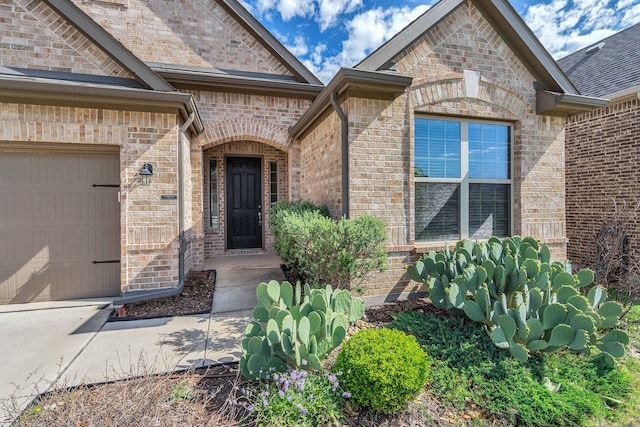 doorway to property featuring concrete driveway, an attached garage, and brick siding