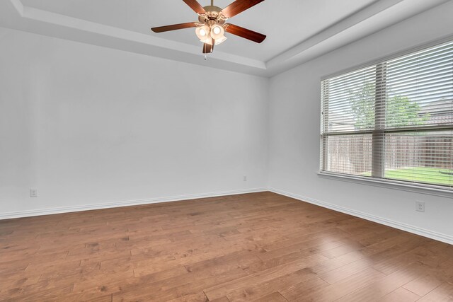 spare room with baseboards, wood finished floors, a ceiling fan, and a tray ceiling