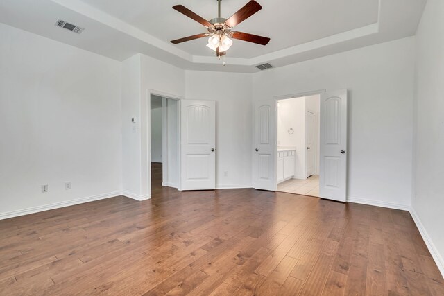 unfurnished bedroom featuring baseboards, visible vents, wood-type flooring, and a tray ceiling