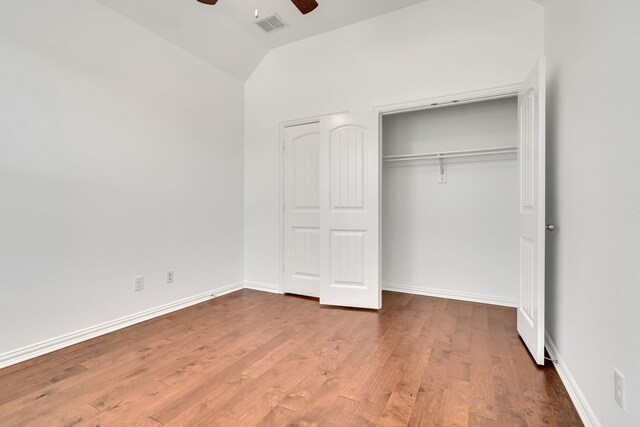 unfurnished bedroom featuring wood finished floors, a closet, visible vents, a ceiling fan, and lofted ceiling