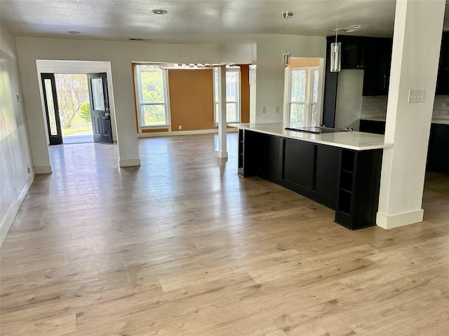 kitchen featuring baseboards, dark cabinetry, open floor plan, and light countertops