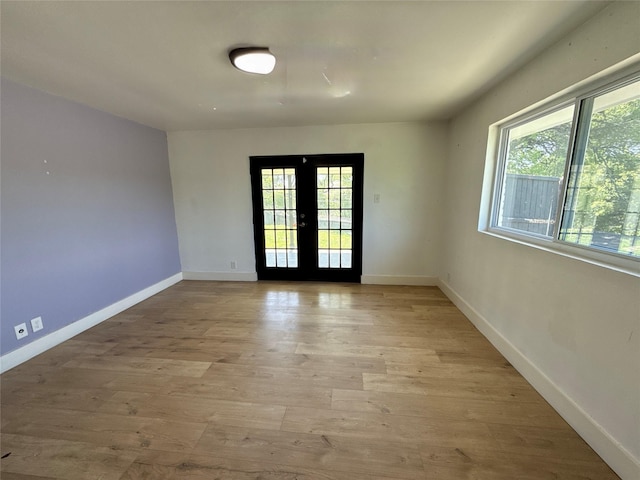 unfurnished room with light wood-style flooring, a wealth of natural light, baseboards, and french doors