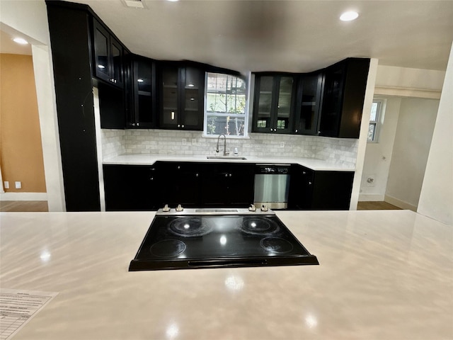 kitchen featuring stainless steel dishwasher, tasteful backsplash, glass insert cabinets, dark cabinets, and cooktop