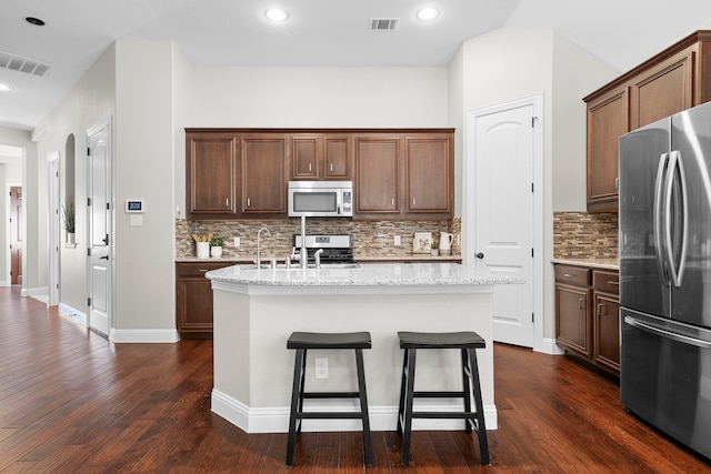 4717 Whitehall Ct, Mckinney, TX 75070 - kitchen with stainless steel appliances, a center island with sink, tasteful backsplash, dark wood-style flooring, and light stone counters