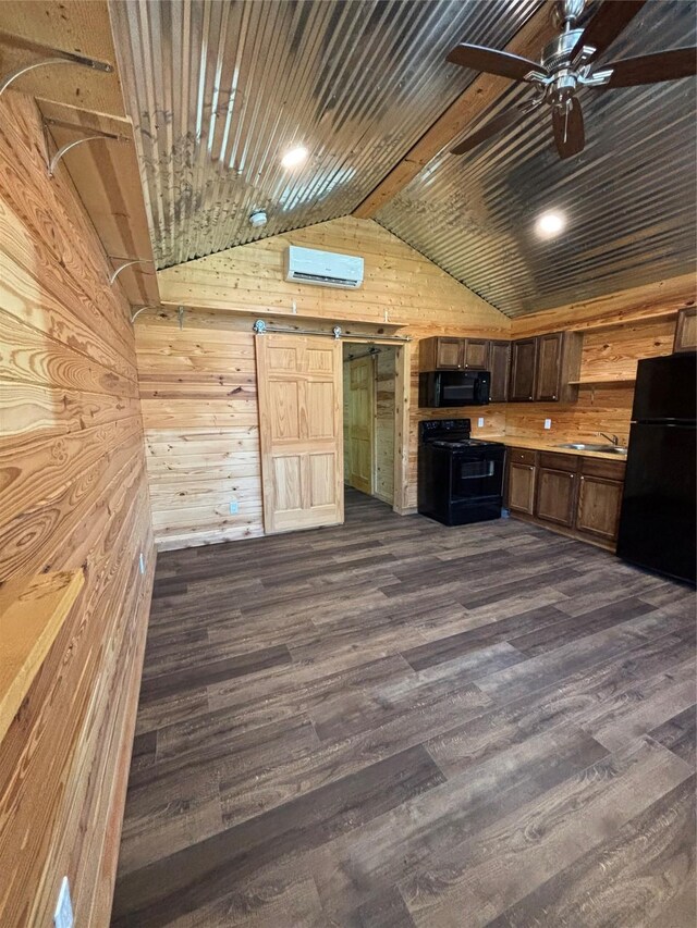 kitchen with vaulted ceiling, wood walls, black appliances, and a barn door