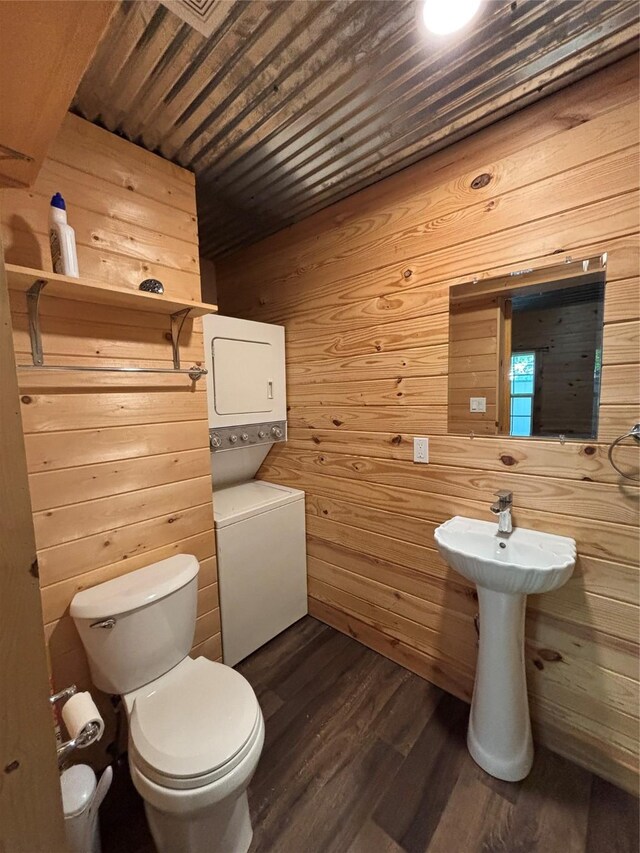 half bath featuring wood finished floors, stacked washing maching and dryer, wooden walls, wooden ceiling, and toilet