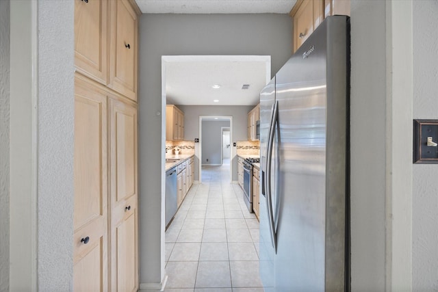 kitchen with stainless steel appliances, light countertops, light brown cabinets, light tile patterned flooring, and decorative backsplash