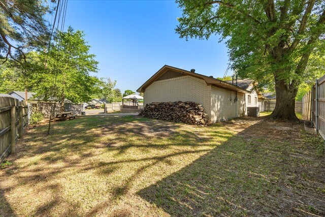 view of side of property with a lawn, central air condition unit, a fenced backyard, and brick siding