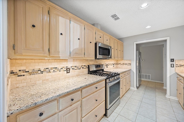 kitchen featuring visible vents, light brown cabinetry, light stone counters, and appliances with stainless steel finishes