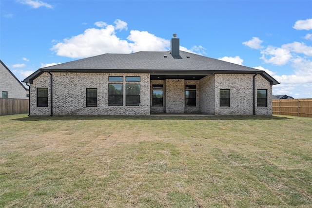rear view of house with brick siding, a lawn, a chimney, and a fenced backyard
