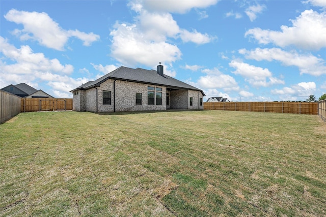 back of house with brick siding, a lawn, a chimney, and a fenced backyard