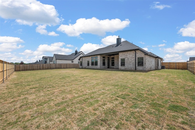 rear view of house with a lawn, a fenced backyard, a chimney, and brick siding