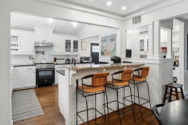 kitchen featuring range with gas stovetop, under cabinet range hood, glass insert cabinets, a breakfast bar area, and white cabinetry