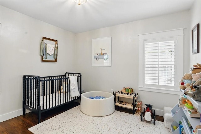bedroom featuring baseboards, a crib, and wood finished floors