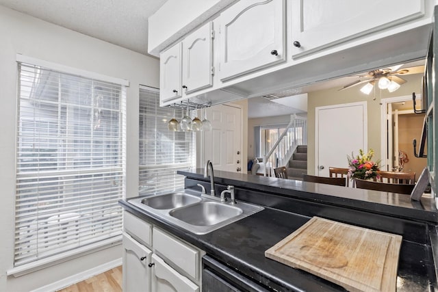kitchen featuring a ceiling fan, dark countertops, a sink, white cabinets, and visible vents