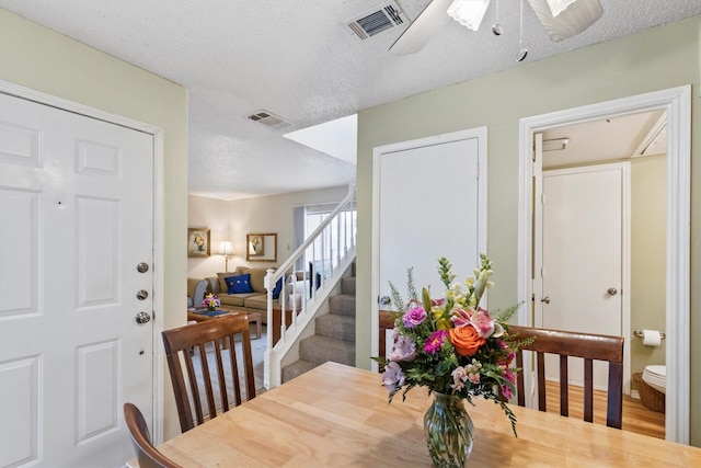 dining space featuring a textured ceiling, stairway, visible vents, and a ceiling fan