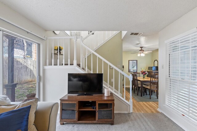 carpeted living room with a healthy amount of sunlight, stairs, ceiling fan, visible vents, and a textured ceiling