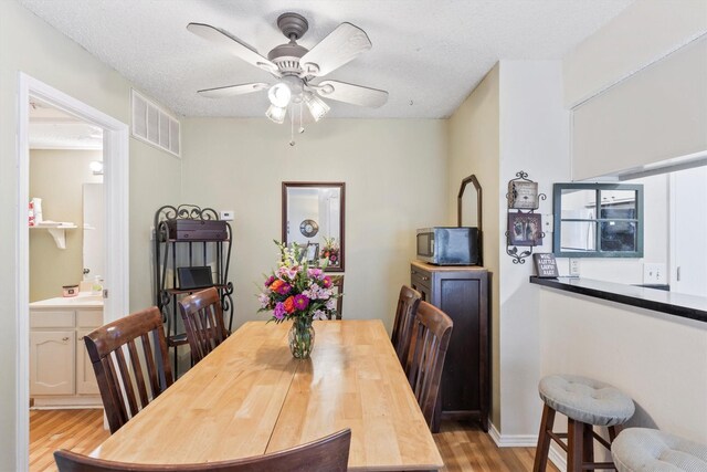 dining space with a textured ceiling, visible vents, a ceiling fan, and light wood finished floors