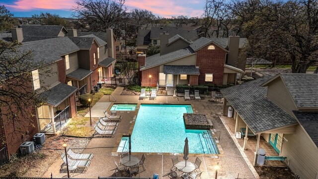 pool at dusk with central air condition unit, a community pool, a patio area, and a residential view