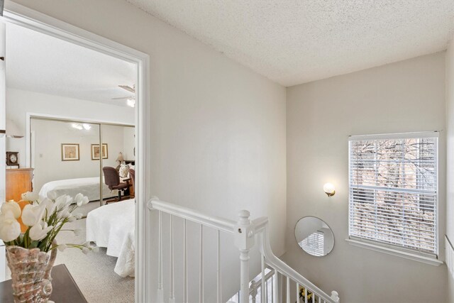 hall featuring carpet floors, a textured ceiling, and an upstairs landing