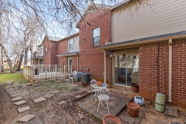 rear view of property with central air condition unit, a wooden deck, brick siding, and a patio area