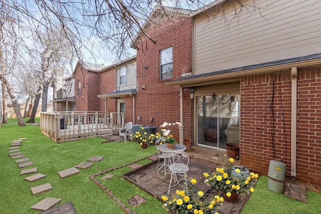 back of house featuring a deck, a yard, brick siding, central AC unit, and a patio area
