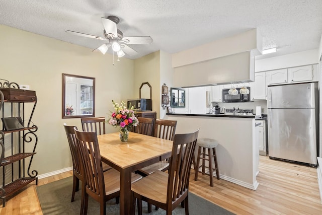 dining space featuring baseboards, light wood-type flooring, ceiling fan, and a textured ceiling
