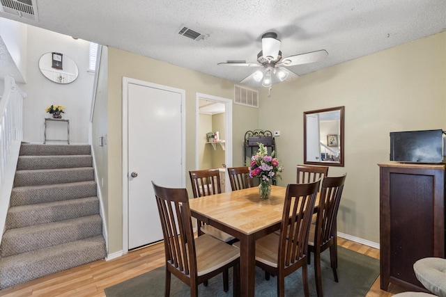 dining space with light wood-style flooring, visible vents, stairway, and a ceiling fan